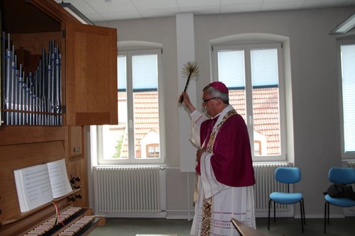 Bischof Wiesemann mit einem Weihwasser-Wedel in der Hand segnet eine Orgel im neuen Haus der Kirchenmusik in Speyer.